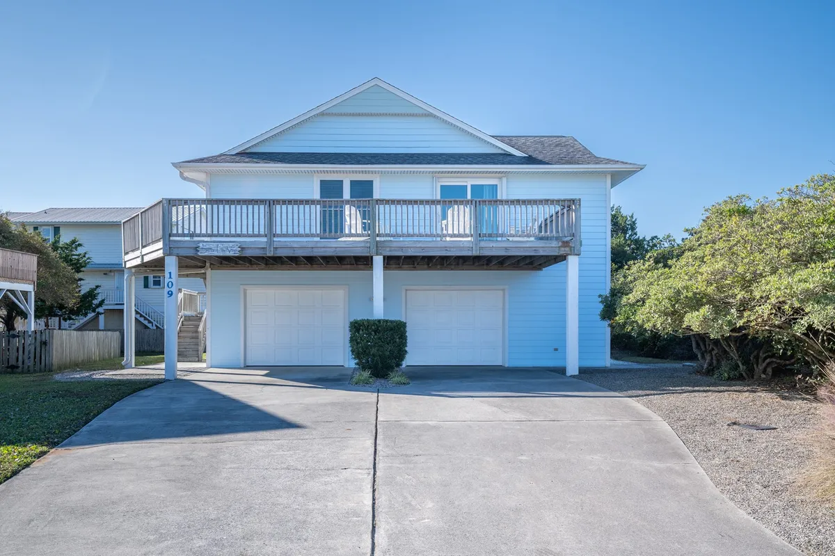 This exterior photo showcases the home’s inviting front balcony, the driveway, lush landscaping, and a welcoming front door. The scene evokes a sense of arrival and anticipation for local adventures, while the comfortable porch hints at relaxing after a day of exploring.