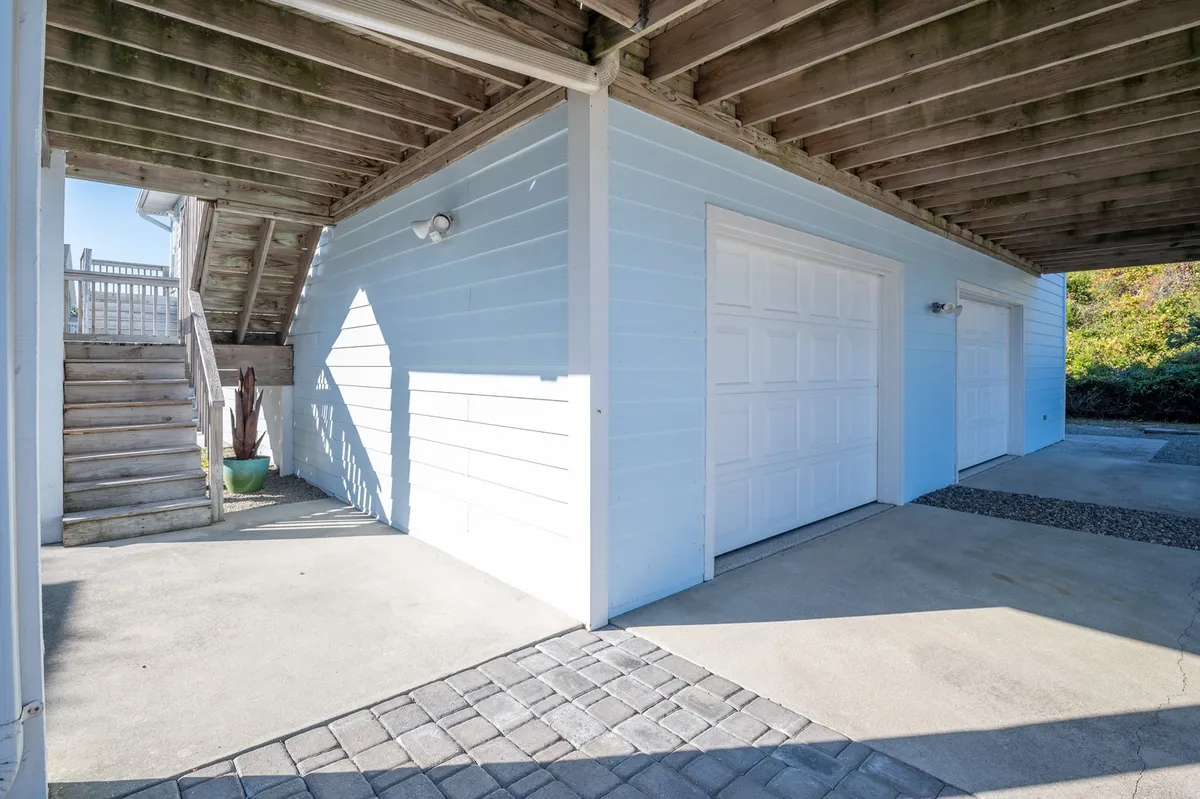 This image captures the exterior of the home with the staircase, garage doors, and blue siding as primary features. The functional aspect of the garage is clearly visible, along with the welcoming entrance and accessible outdoor areas.