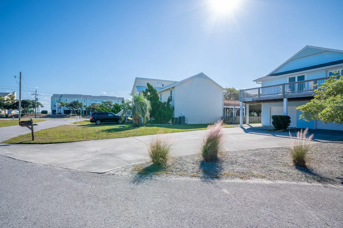 A welcoming exterior shot featuring the spacious driveway, attractive landscaping, and multiple houses in a sunlit setting. The sense of plentiful parking and versatile outdoor space is apparent, reinforcing the property’s capacity to accommodate boats, golf carts, and additional vehicles as mentioned in the section.