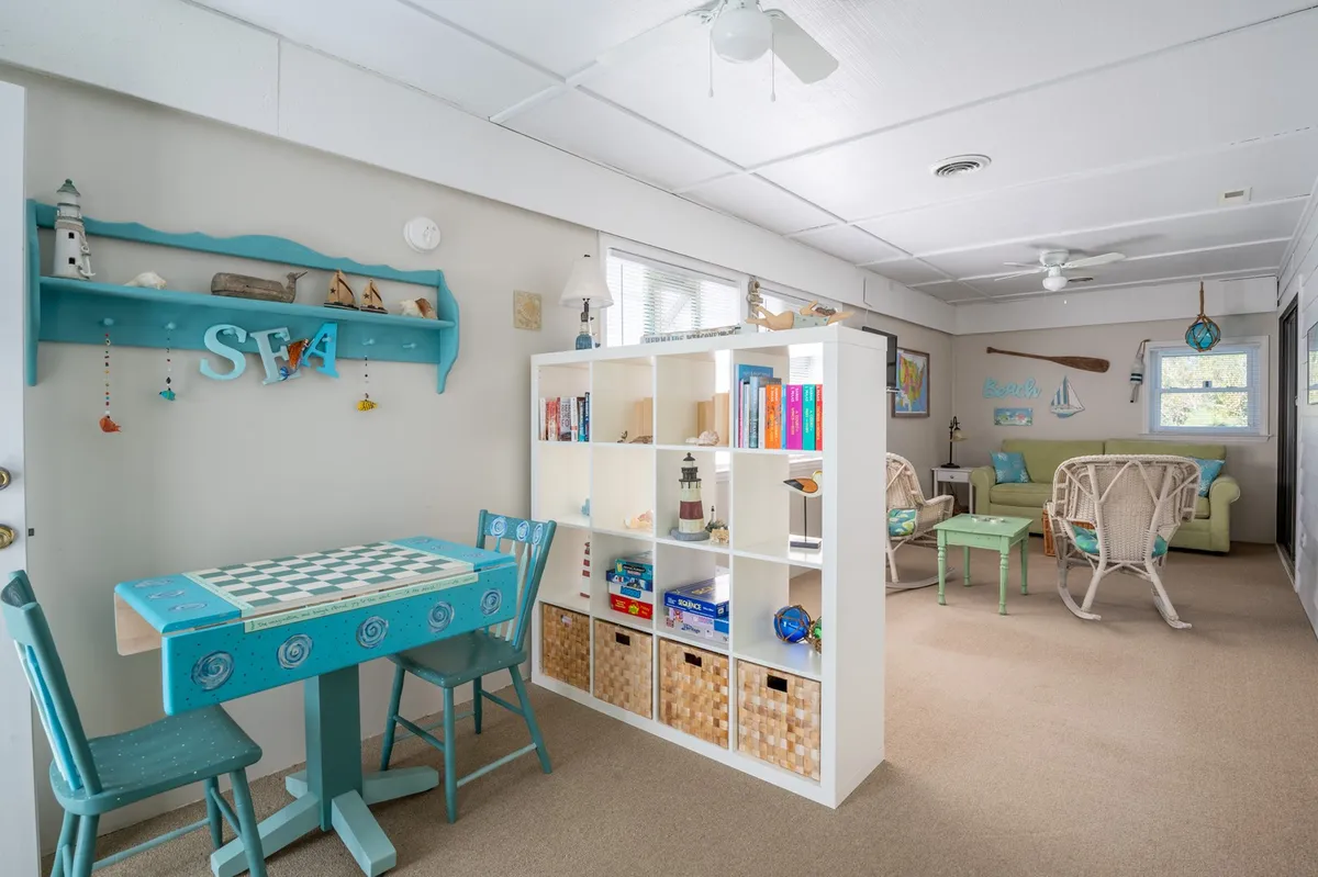 A cheerful interior space with a turquoise table ideal for board games or tea parties, a white bookshelf stocked with books and toys, and a cozy seating area with wicker chairs. The playful and relaxed mood is ideal for family activities and children's gatherings.
