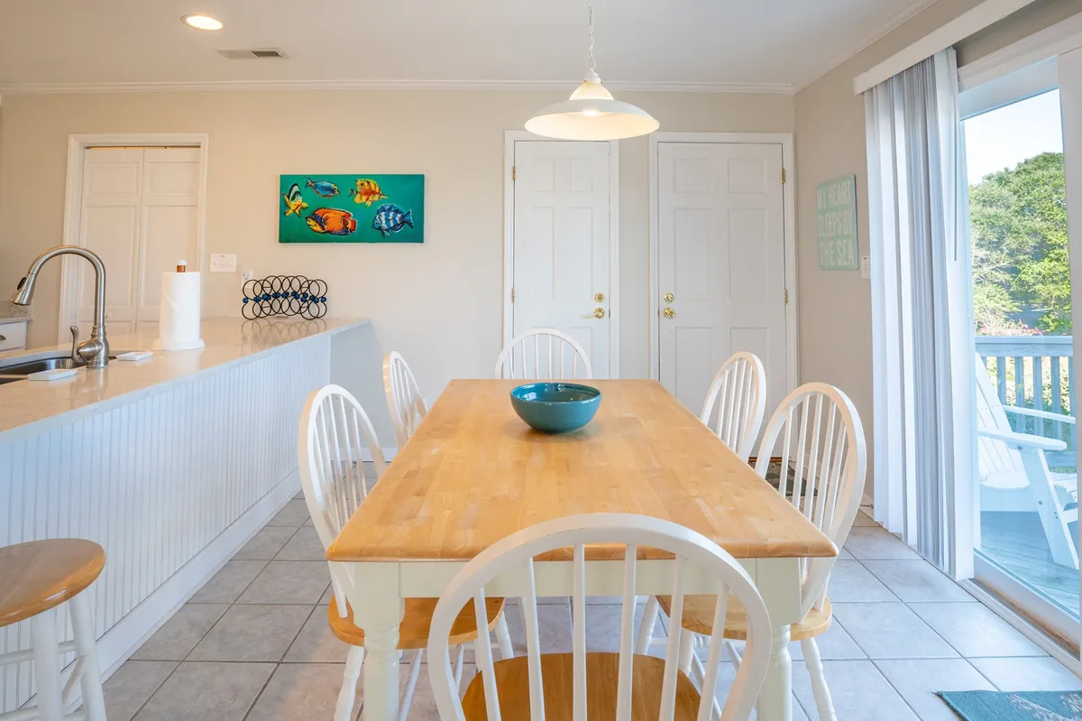 A cozy dining area with a welcoming table set for shared meals, colorful wall art, and the kitchen counter visible in the background. The inviting ambiance suggests a space tailored for family breakfasts, celebratory dinners, or evening games, with easy access between the kitchen and dining zones.