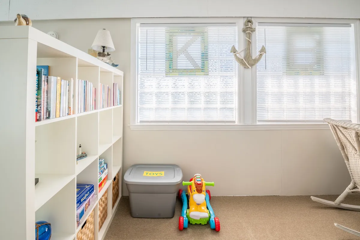 A bright, playful room featuring a bookshelf full of children's books, a colorful toy ride-on vehicle, a storage box for toys, and nautical-themed decor, including a decorative anchor. The space is open and inviting, encouraging reading, creative play, and storytelling for young children.