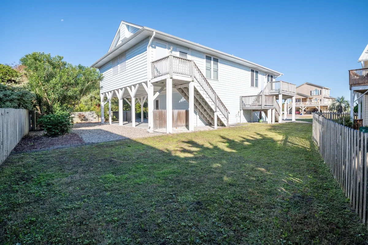A welcoming exterior perspective showing an elevated deck, a staircase leading down to a landscaped and partially fenced yard, and plenty of open space for play and relaxation. The yard features are visible, creating a sense of a private outdoor oasis.