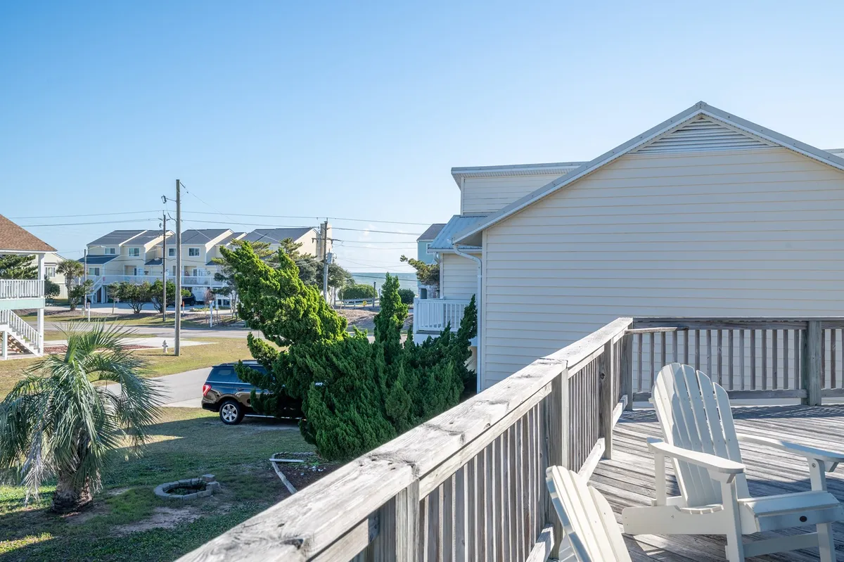 A serene view from the deck, with Adirondack chairs overlooking lush greenery and the beach beyond. This outdoor living space is ideal for enjoying ocean glimpses and breezy indoor-outdoor living as described in the section, connecting the interior gathering spaces to the tranquil wrap-around porch.