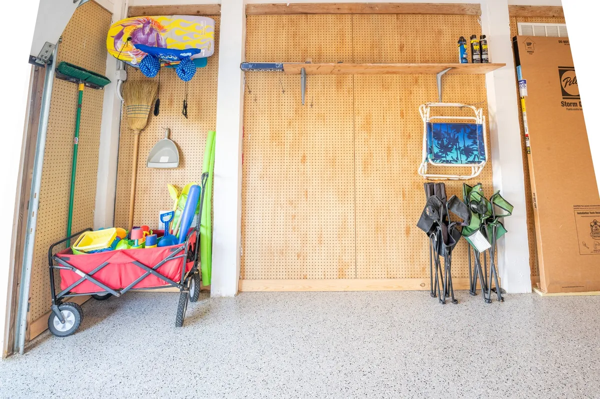 A functional and playful storage area displaying colorful beach gear, a red wagon, and a pegboard wall with organized tools, ready for spontaneous adventures. The space is tidy yet lively, emphasizing the cottage’s proximity to beach activities.